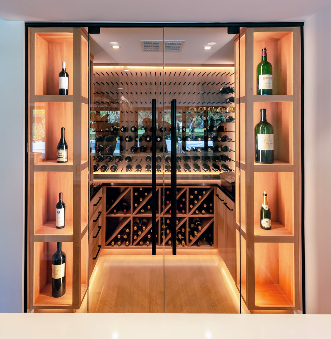 Modern wine cellar with wooden shelves and glass doors displaying various bottles of wine.